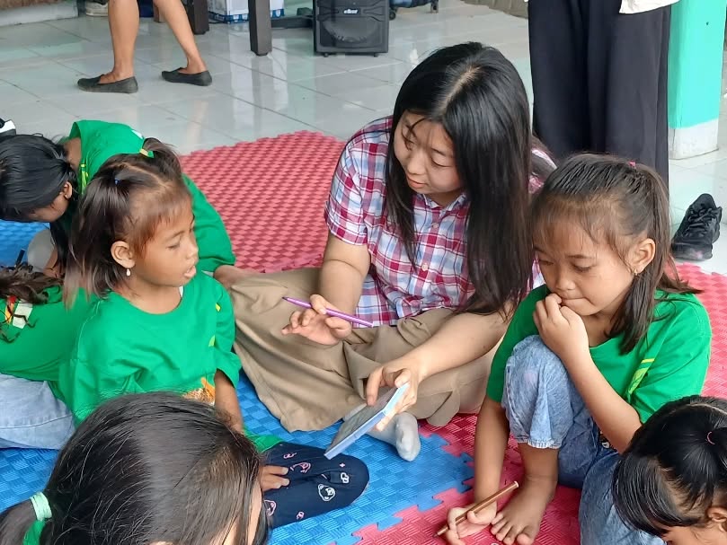 Relawan mendampingi dua anak menggambar di atas matras