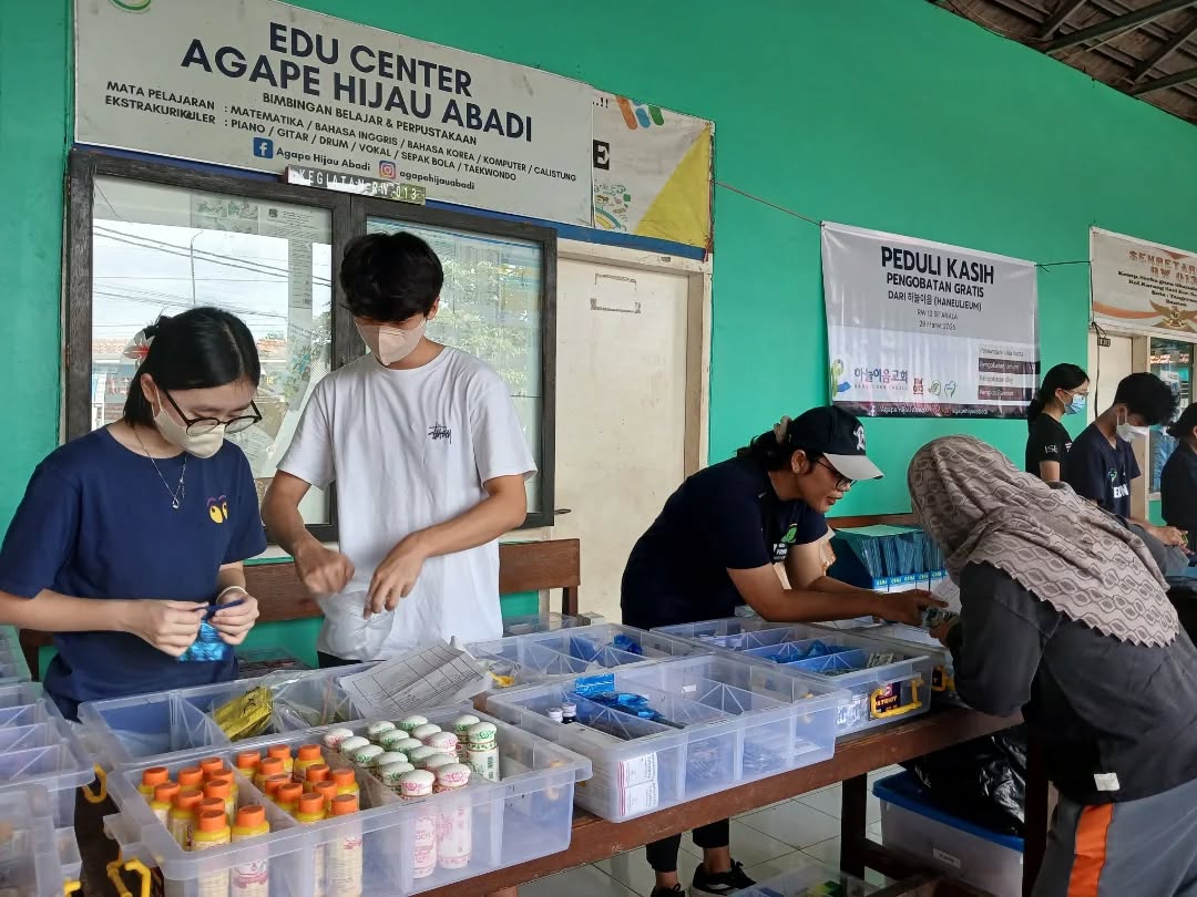 Papan nama Edu Center Agape Hijau Abadi dan relawan menyiapkan obat untuk layanan pengobatan gratis