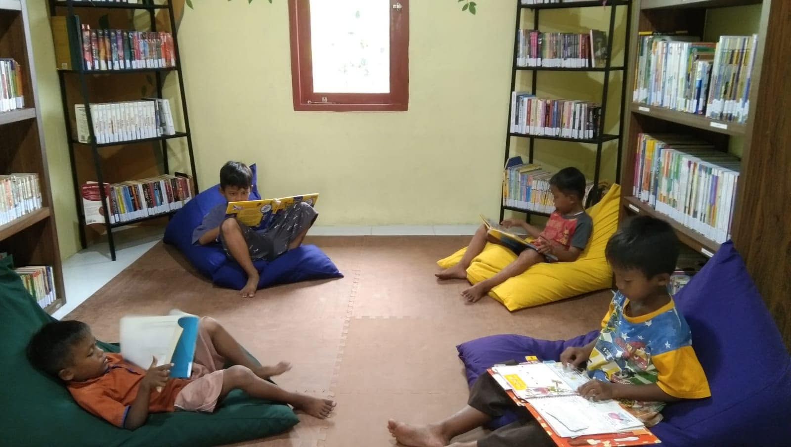 Ruang perpustakaan anak di kampung Sitanala dengan rak buku di sekeliling ruangan