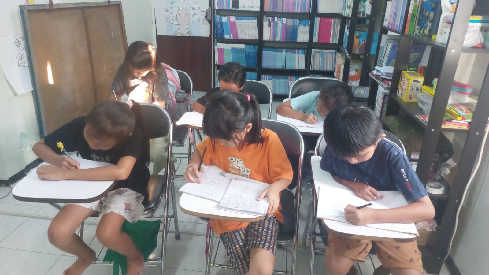 Anak-anak mengerjakan tugas sekolah di meja perpustakaan